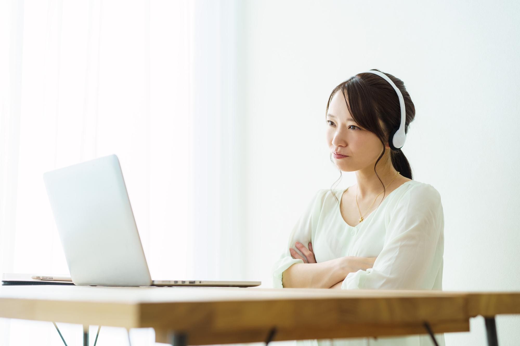ヘッドセットを着けて、ノートPCに向かって腕組みをする若い女性
