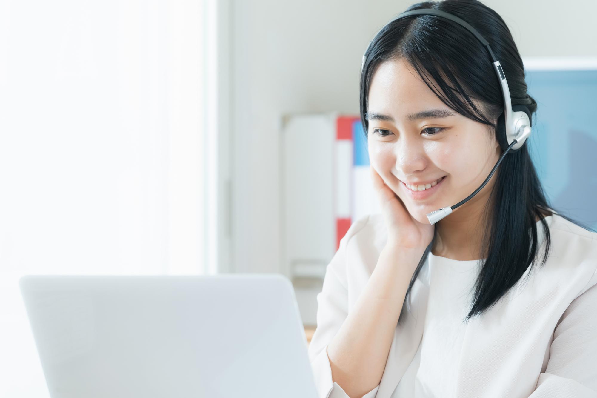 ノートPCに向かい満足そうな笑顔を浮かべるヘッドセットを着けた若い女性