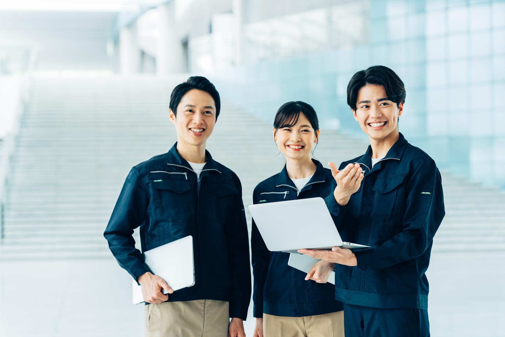 ノートPCを携え微笑む、清潔な作業服を着た3人の男女